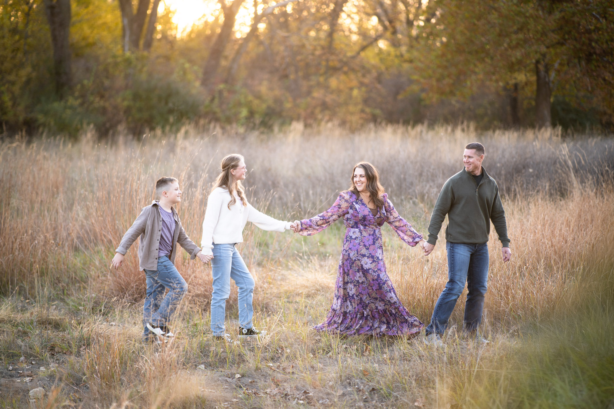 A family of four walking hand in hand through a sunlit field