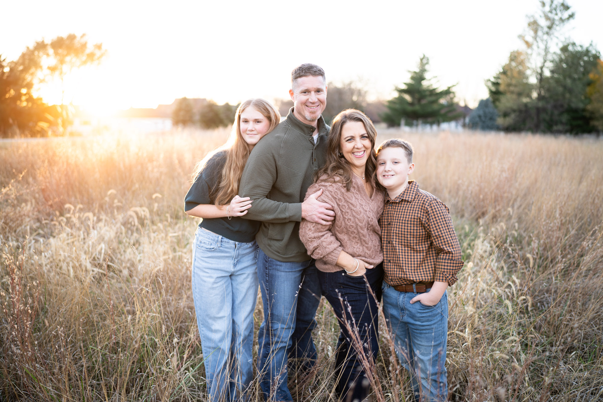 A family of four standing close together in a field at sunset
